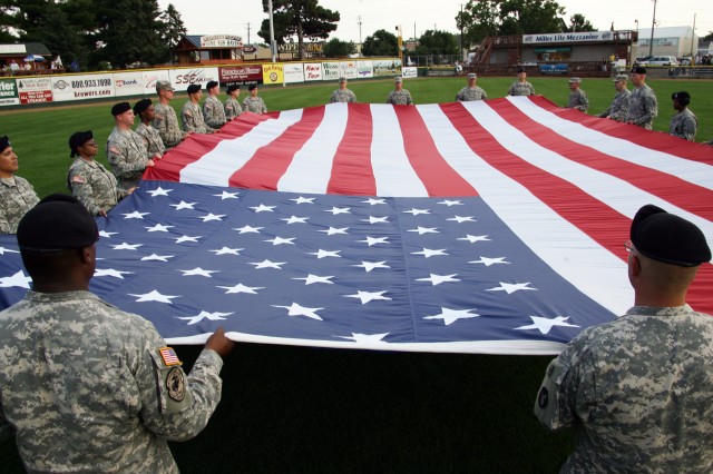 Soldiers from the 33rd Brigade Combat Team and the 81st Brigade Combat Team hold a large U.S. Flag during opening ceremonies at the Military All-Stars versus La Crosse All-Stars baseball game.