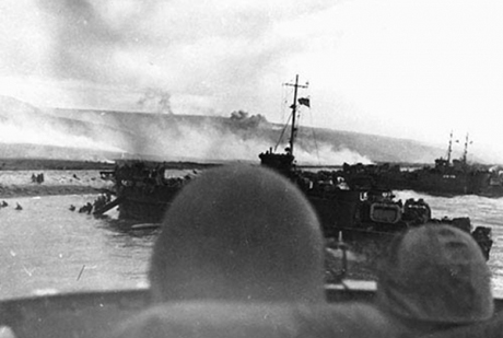 Soldiers and crewmen aboard a Coast Guard landing craft approach Normandy.