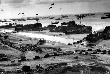 Soldiers in cargo vehicles move onto a beach in Normandy