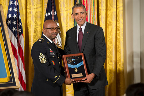 President Barack Obama bestows the Medal of Honor to Sgt. Henry Johnson, accepting on his behalf is Command Sgt. Maj. Louis Wilson, of the New York National Guard, in the East Room of the White House, June 2, 2015. Then-Pvt. Johnson, an African-American, distinguished himself as a member of 369th Infantry Regiment "Harlem Hellfighters," 93rd Division, American Expeditionary Forces, during combat operations against the enemy on the front lines of the Western Front in France during World War I. While on night sentry duty, May 15, 1918, Johnson and a fellow Soldier, Pvt. Needham Roberts, received a surprise attack by a German raiding party consisting of at least 12 soldiers. While under intense enemy fire and despite receiving significant wounds, Johnson mounted a brave retaliation resulting in several enemy casualties. When his fellow Soldier was badly wounded, Johnson prevented him from being taken prisoner by German forces. Wielding only a knife and being seriously wounded, Johnson continued fighting, took his Bolo knife and stabbed it through an enemy soldier's head. Displaying great courage, Johnson held back the enemy force until they retreated. The "Harlem Hellfighters" were the first all-black regiment that helped change the American public's opinion on African-American Soldiers that helped pave the way for future African-American Soldiers. U.S. Army photo by Staff Sgt. Bernardo Fuller