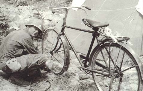 Chaplain Emil Kapaun fixes a flat on his bicycle in Korea, August 1950. Kapaun often rode this bike from location to location along the fighting lines to visit soldiers. (Photo courtesy Col. Raymond Skeehan)