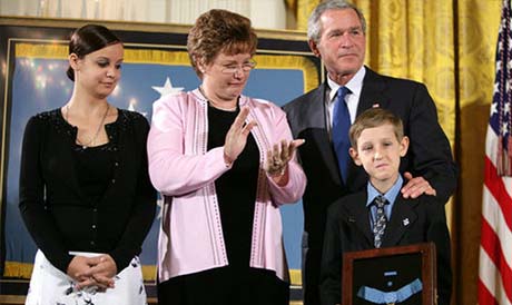 President George W. Bush places his hand on the shoulder of 11-year-old David Smith after he presented the young man with the Medal of Honor, awarded his father, Sgt. 1st Class Paul Smith, posthumously during the ceremony at the White House April 2005. Joining David on stage are his step-sister Jessica and his mother, Birgit Smith. Photo by Eric Draper.