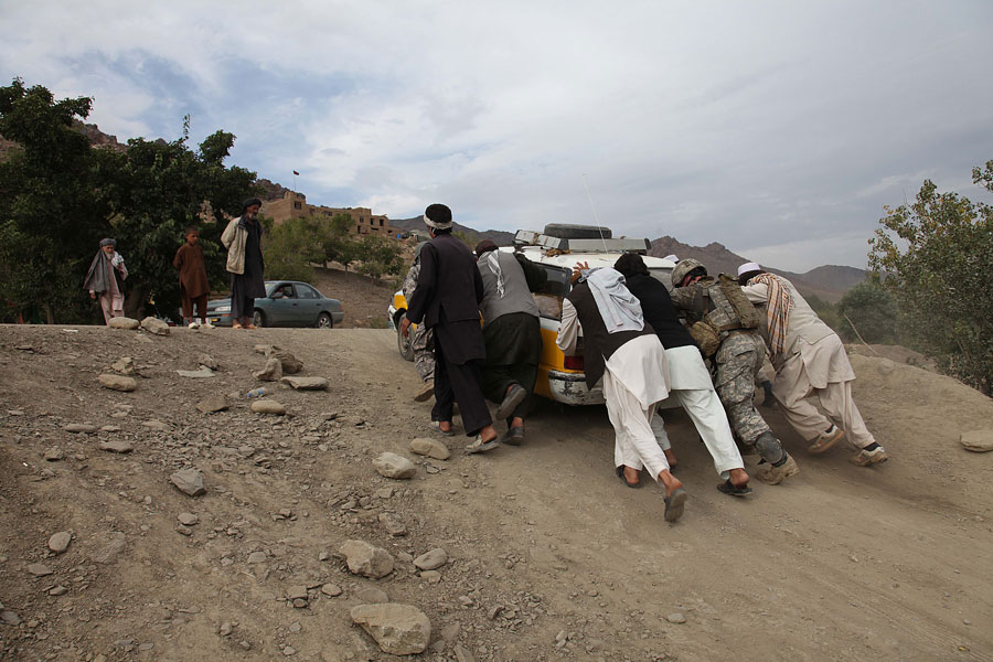 Soldiers help push an Afghan vehicle up hill