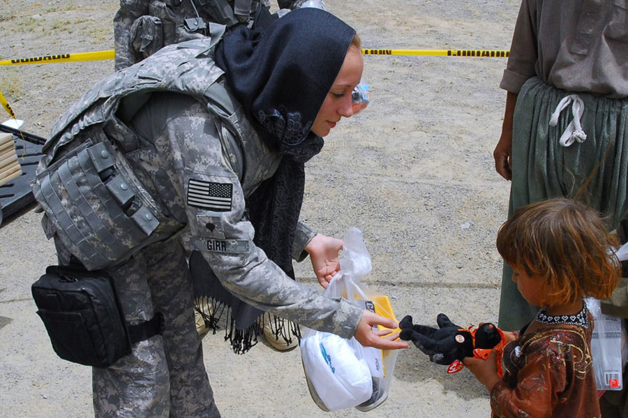 Soldier hands stuffed bear to young Afghan girl during humanitarian assistance mission