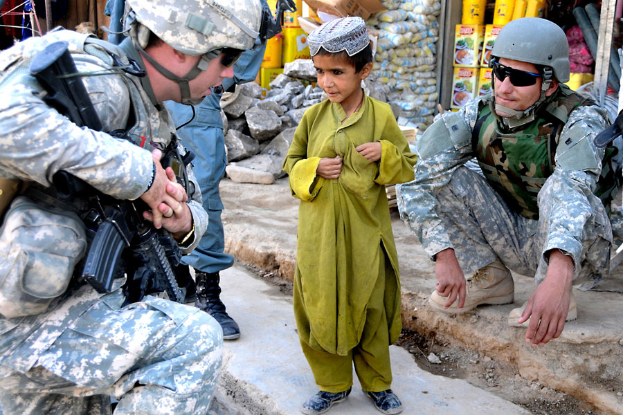 Afghan National Interpreter and Soldier from White Tank talk with Afghan boy during a patrol at a bazaar