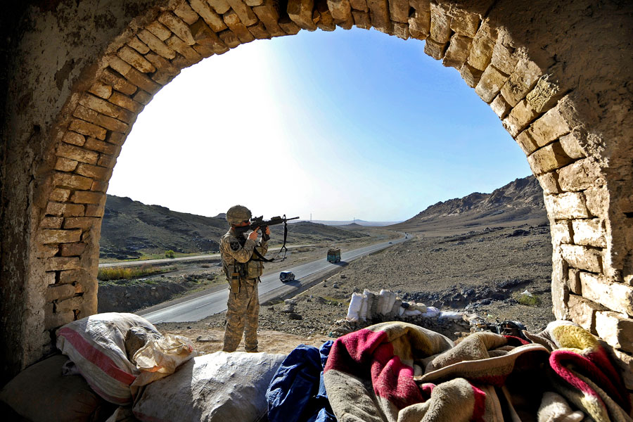Soldier uses rifle scope to scan hill while providing security outside Afghan police checkpoint