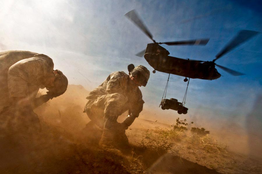 Staff Sergeant Hector Hoyas and Senior Airman Matthew Phillips turn away from the CH-47 Chinook helicopter prop wash