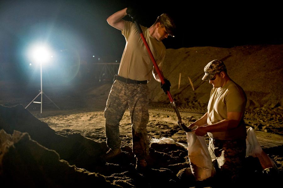 Specialist Benjamin Sukys and Specialist Robert Thorp work through the night filling sandbags