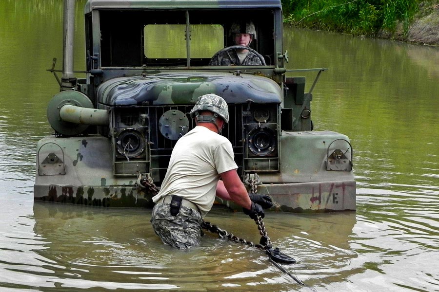 Staff Sergeant Keith Ericson checks the cable connection of a vehicle stranded in water during a training exercise while Specailist Andrew Miller steers the vehicle