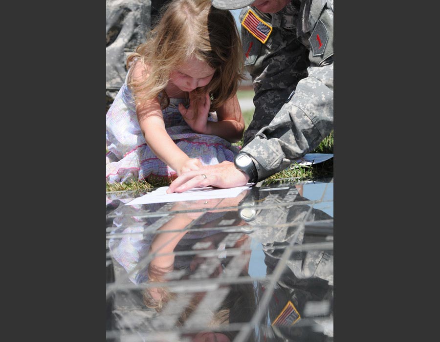 Hannah Maher makes a rubbing of the memorial stone honoring her dad, Sergeant Brent Maher, following the Victory Park Ceremony at Fort Riley, Kansas