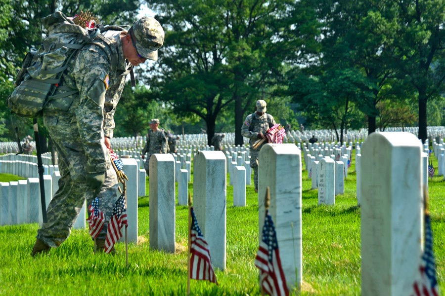 A Soldier of the 3rd United States Infantry Regiment (The Old Guard) places small American flags in front of a headstone in Arlington National Cemetery, Virginia