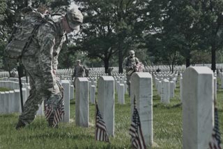 A Soldier of the 3rd United States Infantry Regiment (The Old Guard) places small American flags in front of a headstone in Arlington National Cemetery, Virginia