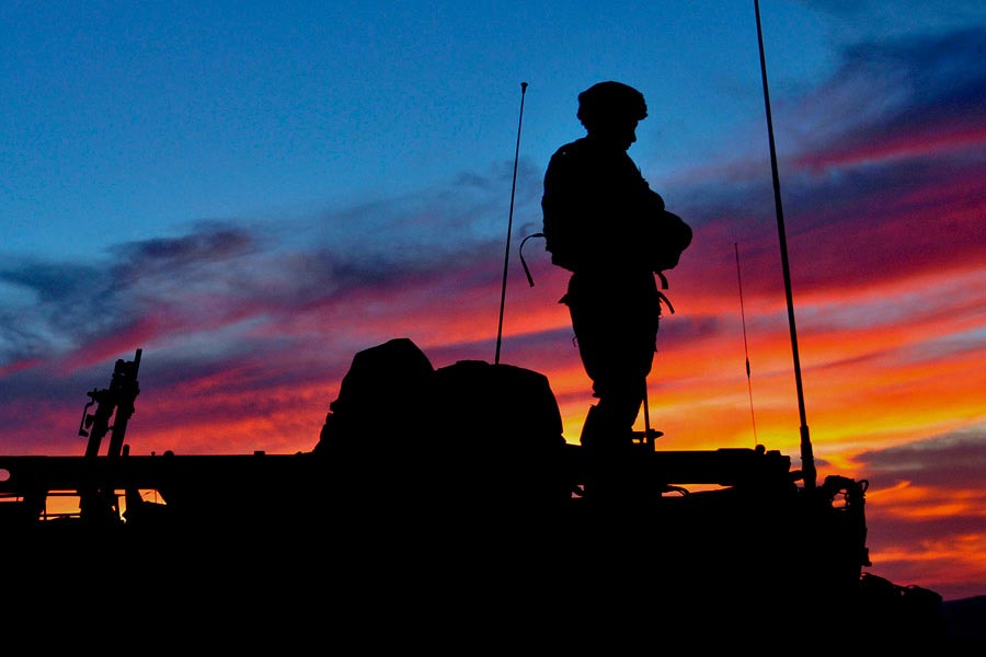 Soldier standing on Styker armored fighting vehicle at sunset