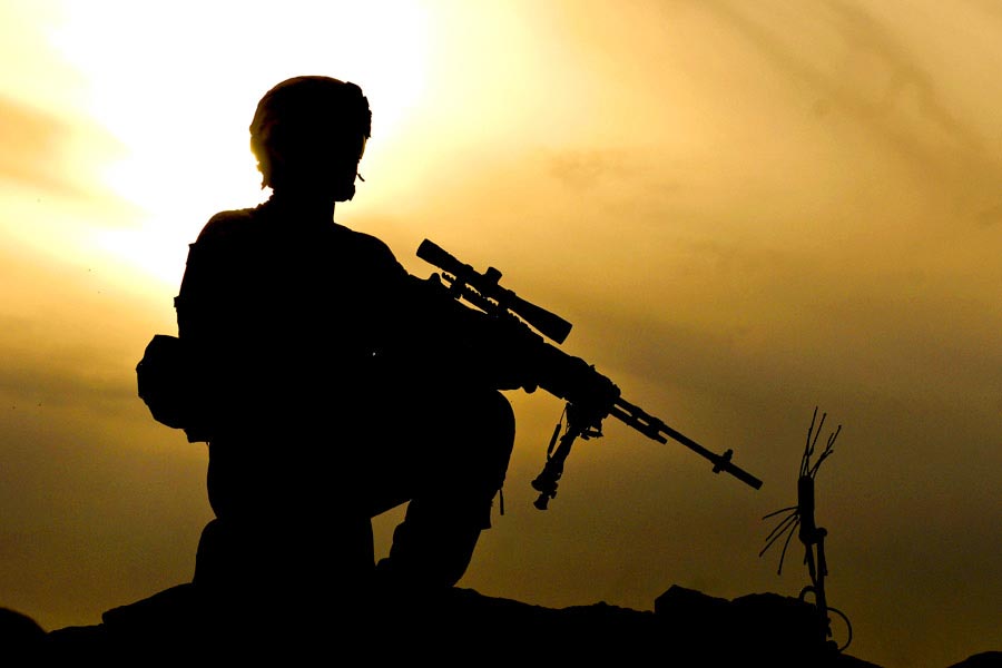 Private First Class Kevin March kneels on cliff providing security for his squad