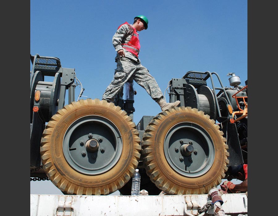 Private First Class Andrew Coffman inspects a load of heavy equipment on a flatbed truck prior to shipping it out of the country